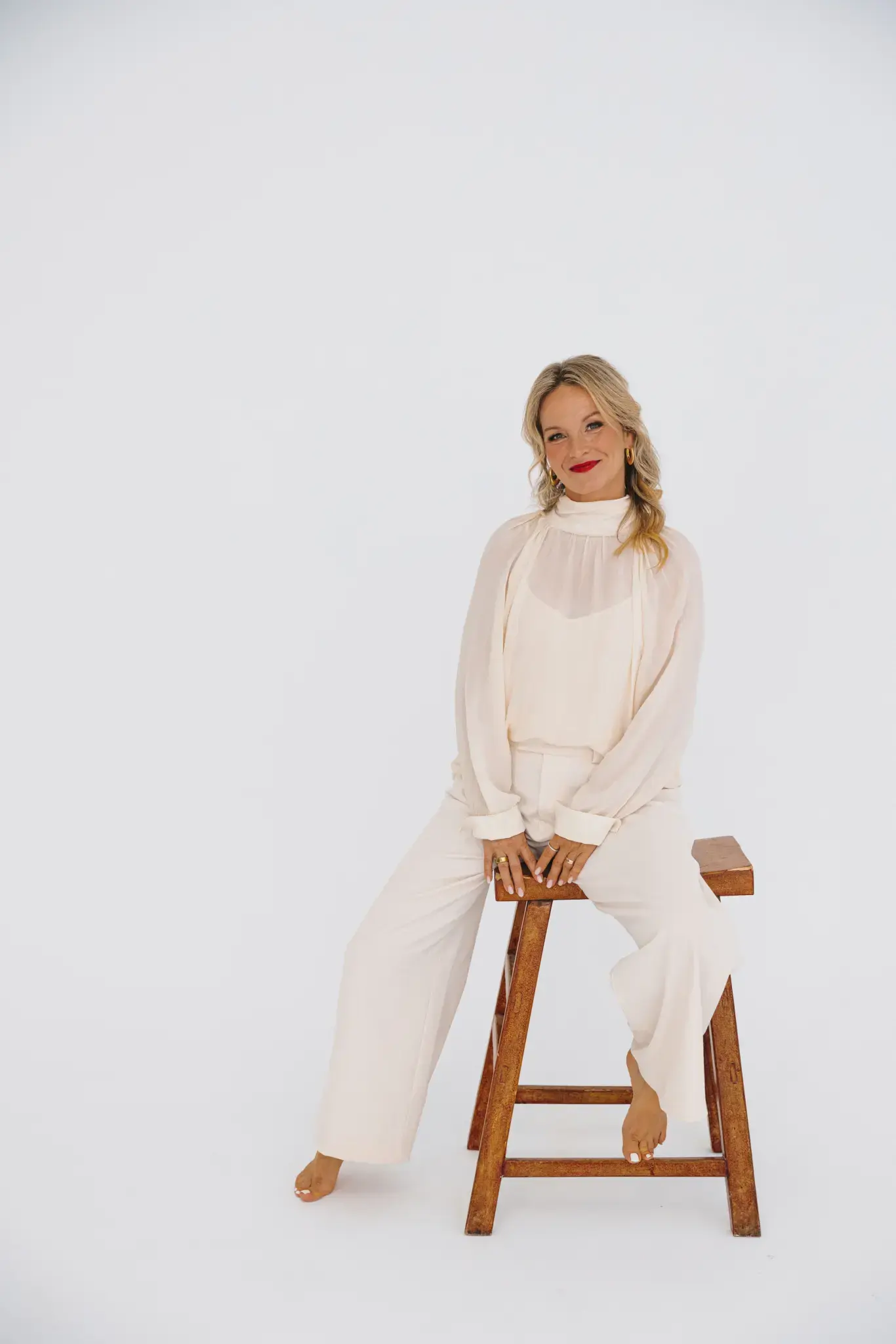 Korinna Söhnholz sitzt auf einem Holzhocker und lächelt in die Kamera