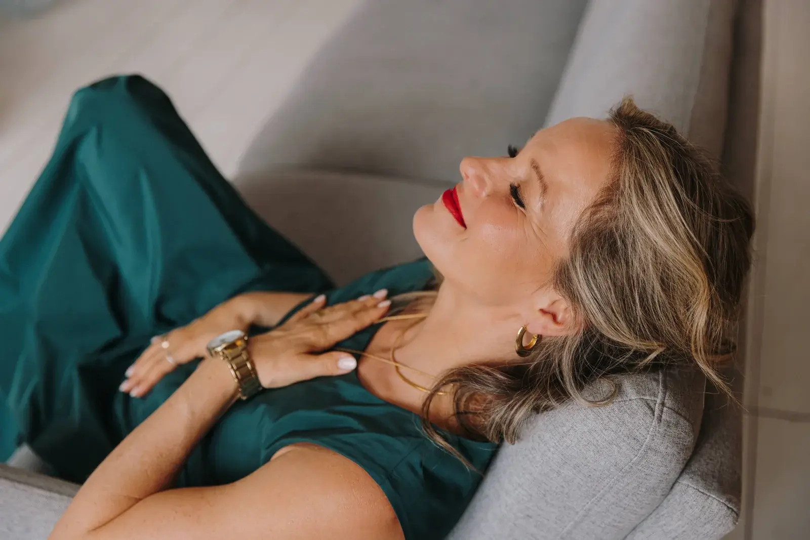 Korinna Söhnholz im grünen Kleid entspannt auf dem Sofa, die Hände auf dem Herzen