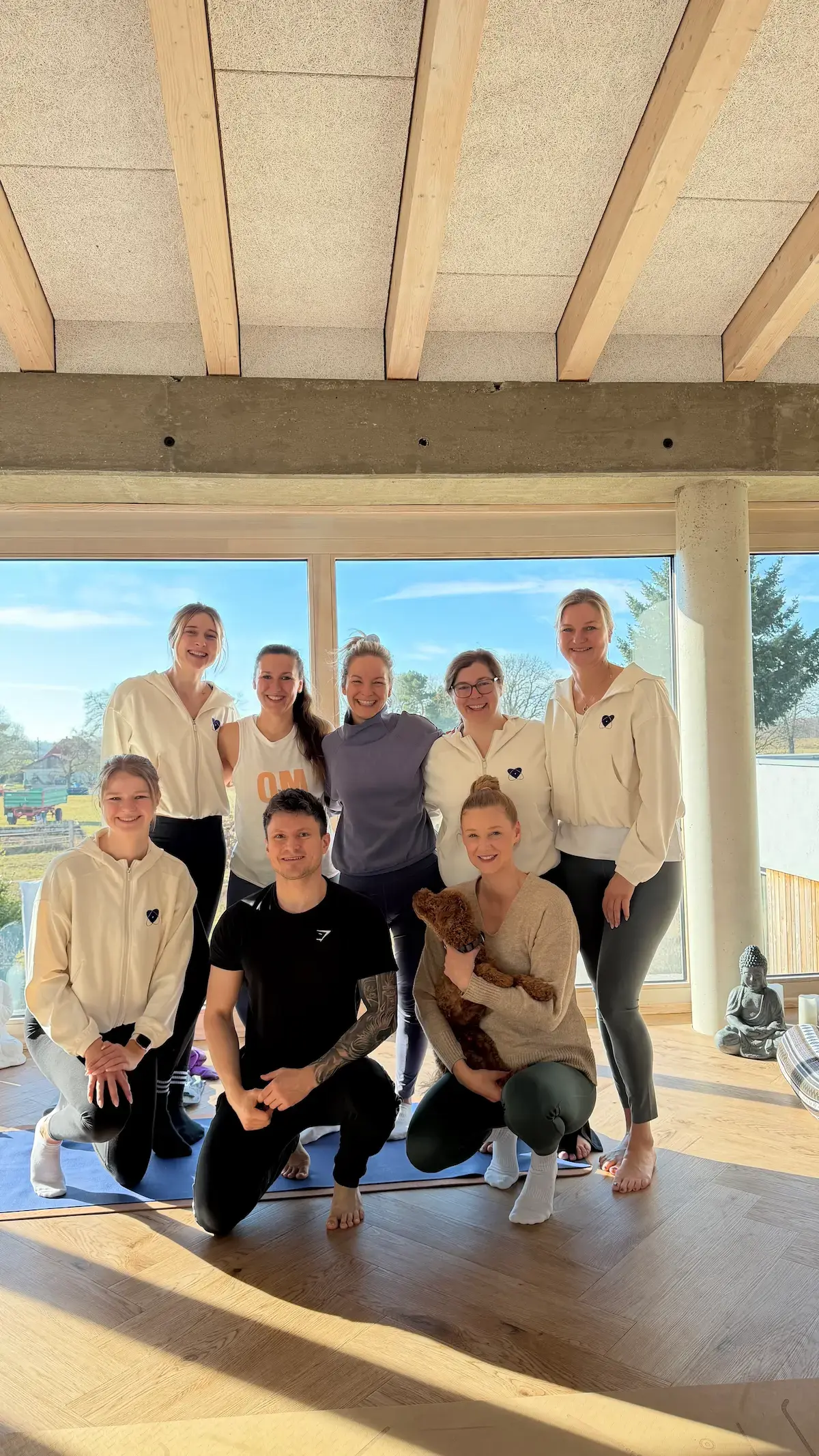 Das Team steht und kniet zusammen im hellen Studio und lacht in die Kamera